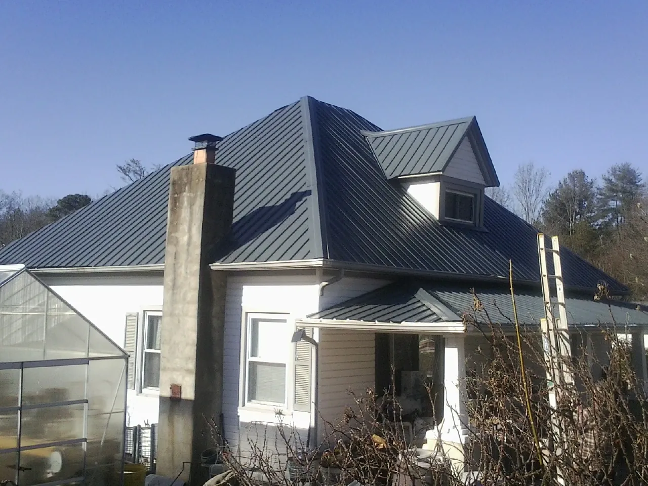 Dark blue standing seam metal roof on a white farmhouse with dormer — Slate & Tile Roof Repair by Roofing Brothers in Wheat Ridge
