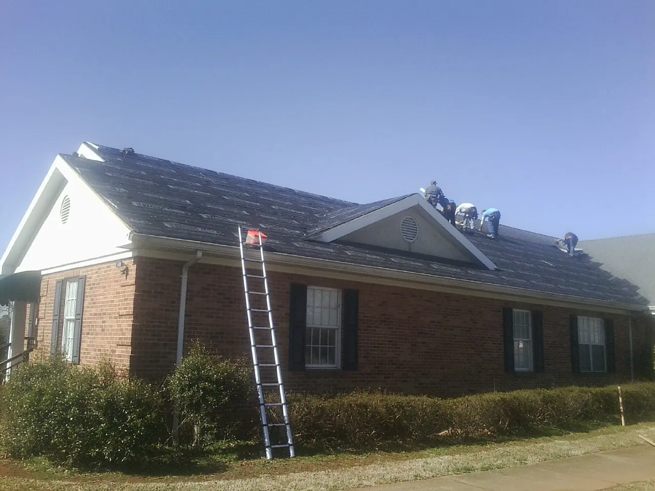 Crew tearing shingles off a brick ranch roof with a ladder set — Emergency Roof Repair work by our crew in Wheat Ridge