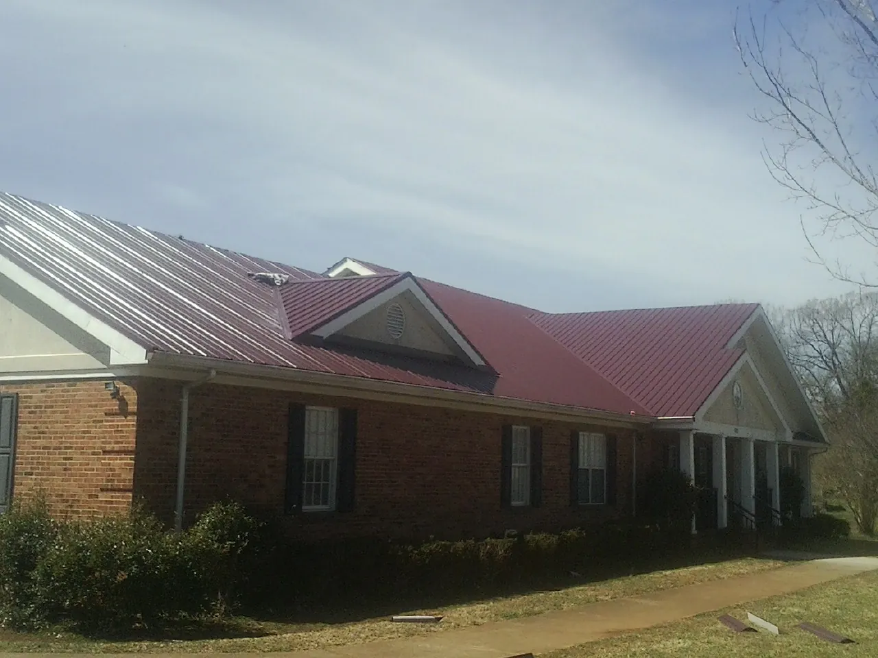 Red metal roof with gabled entries on a long brick building, from a Hail Damage Roof Repair job in Wheat Ridge