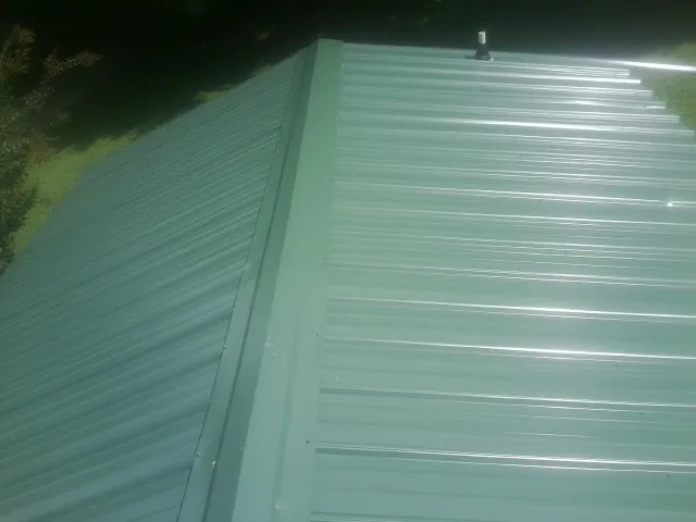New green metal panels meeting at the ridge of a roof — Flat Roof Repair work by our crew in Wheat Ridge