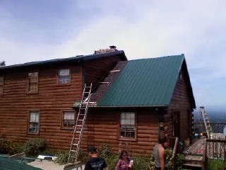 Green metal roof going on a two story log home with ladders set in Wheat Ridge