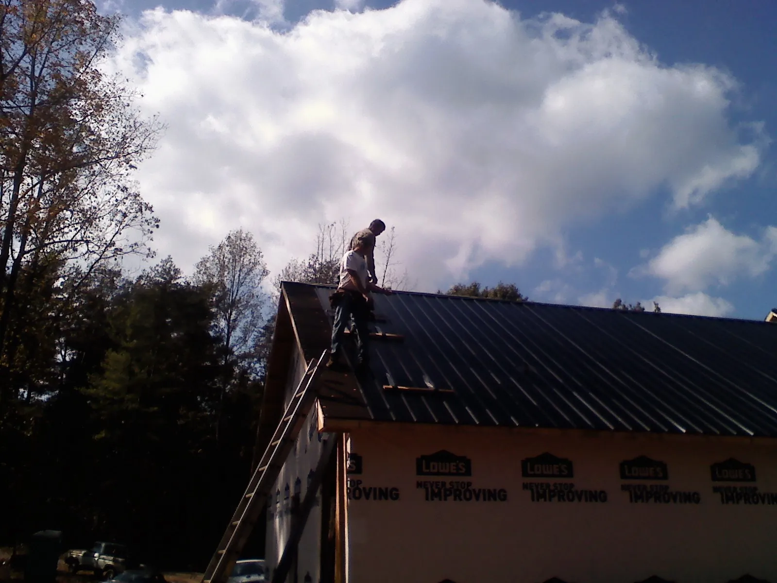 Roofer fastening dark metal panels high against a cloudy sky, from a Roof Inspection job in Wheat Ridge