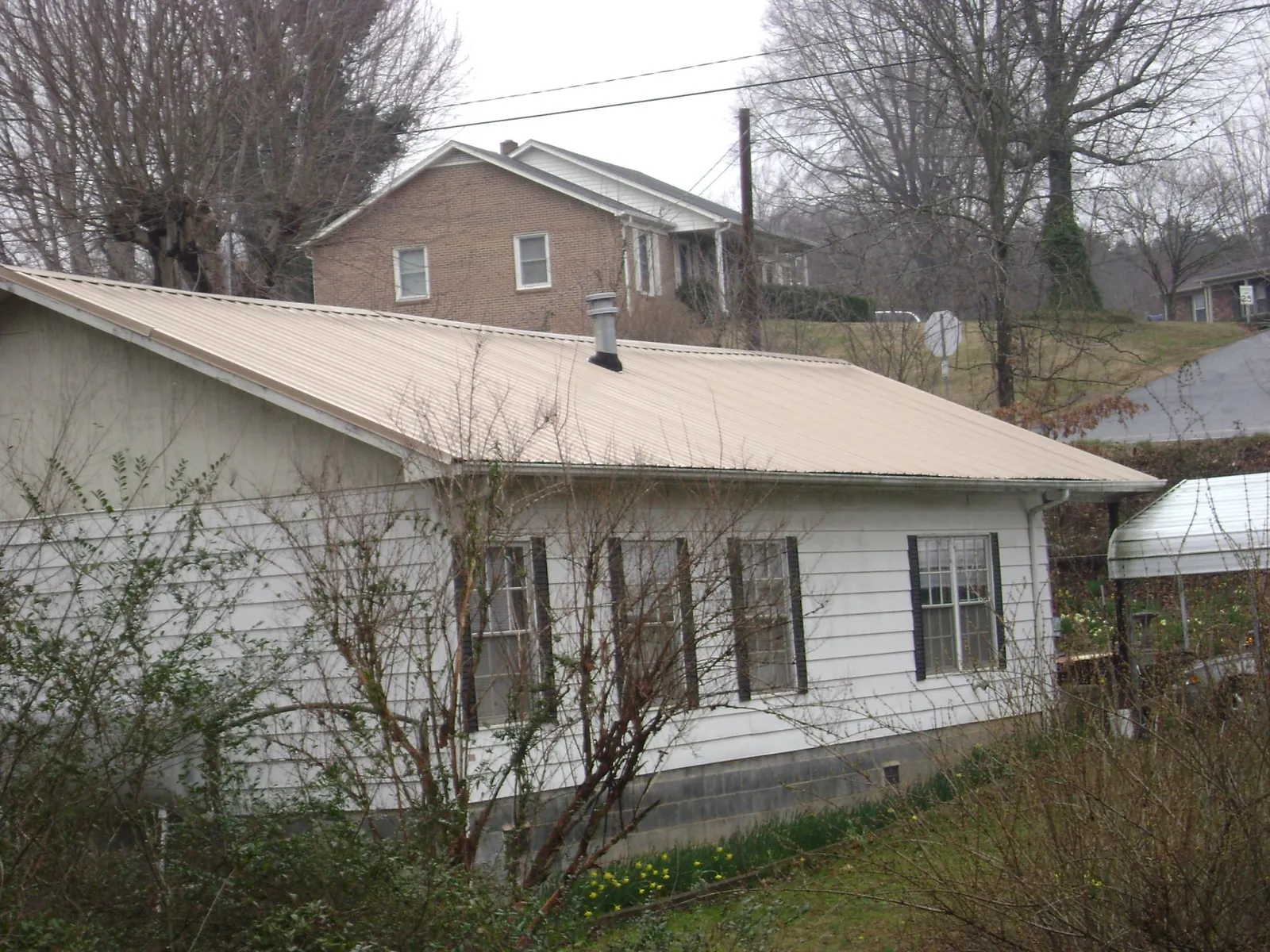 Tan metal roof on a white sided house set into a hillside — Commercial Roofing by Roofing Brothers in Wheat Ridge